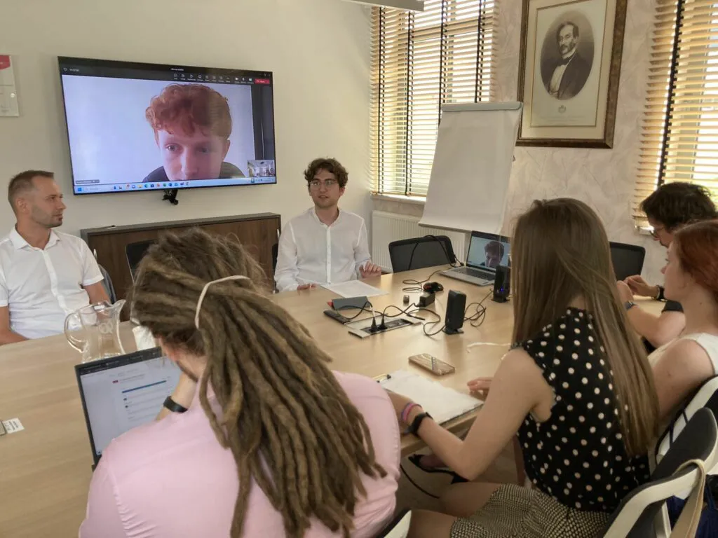 Sześć osób przy stole, siódma na ekranie