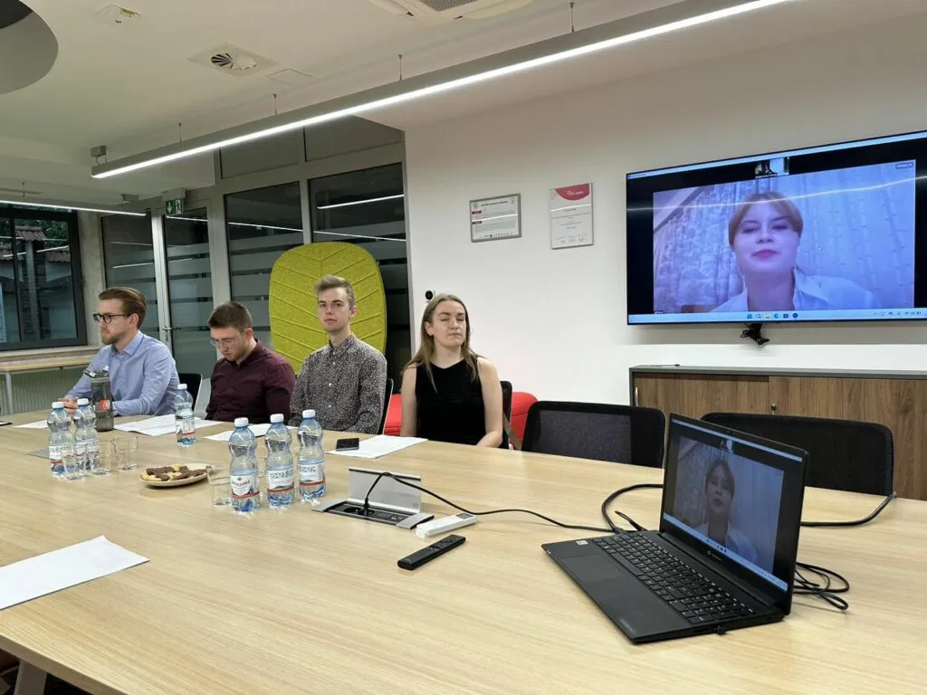 Cztery osoby przy stole, piąta na ekranie