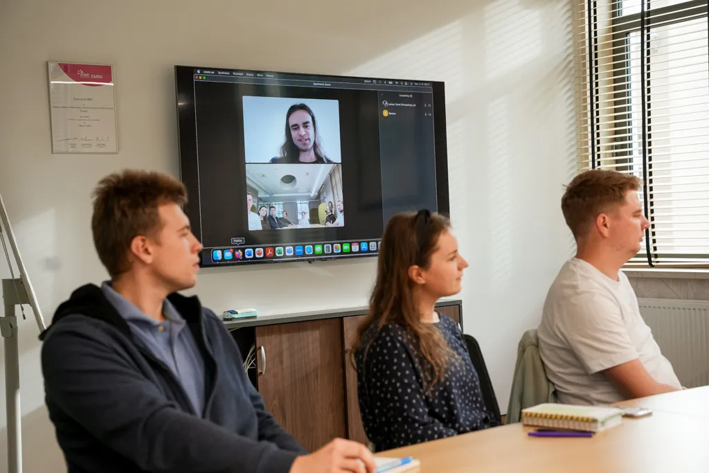 Trzy osoby przy stole, czwarta na ekranie